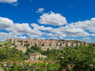 Medieval ancient city wall, battlements, tower, bastion and castle walls of Avila, Spain, around the modern town and buildings, made of yellow stone bricks on a sunny summer day with some clouds