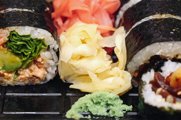 Pickled ginger and wasabi closeup. Fresh garnish on sushi tray. Yellow ginger slices texture. Green wasabi paste detail. Japanese condiment food background. Spicy flavor accent on plate.