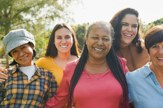 Group of multi generational women hugging each other while smiling on camera at city park - Multiracial female community, friendship and diverse people concept