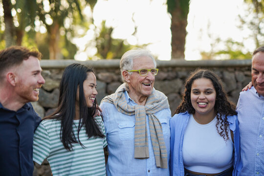 Group of multiracial people with different ages hugging each other outdoor with city park in background - Multi generational community and social gathering concept