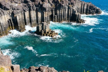Basalt columns along a rugged coastline with turquoise ocean waves crashing against the rock formations