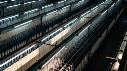 Interior view of a textile factory with rows of spinning machines and illuminated production lines