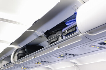 Aircraft overhead bin interior. Open luggage compartment detail. Carry on suitcases stored above seats. Airplane cabin storage space. Travel baggage safety concept. Passenger flight interior view.