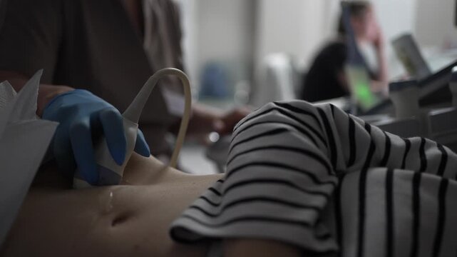 Close-up of a pregnant woman undergoing an ultrasound scan by a gynecologist in a clinic, focusing on the transducer moving over her bare belly during the routine medical examination