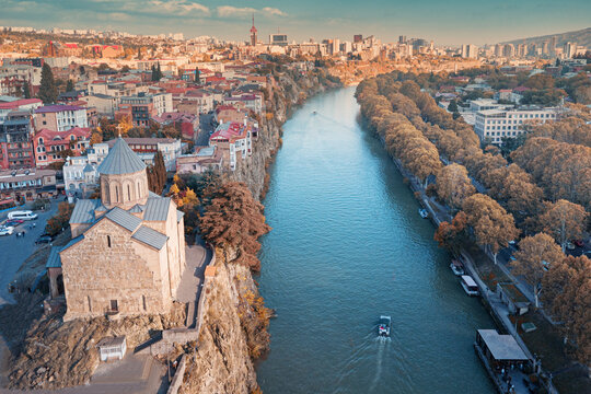 Aerial view of Tbilisi old town and its historic Metekhi church, with the Mtkvari river flowing through the vibrant urban landscape during autumn