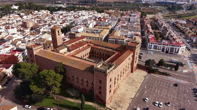 Slow push-in aerial shot toward the historic Santa Maria monastery, revealing its fortified walls and the surrounding town of El Puig in Valencia