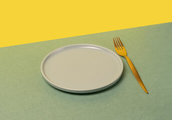 Round blue plate and golden fork on green and yellow background, space for text