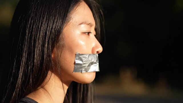 Young Asian Woman with Duct Tape Over Mouth Symbolizing Silenced Voice and Censorship.