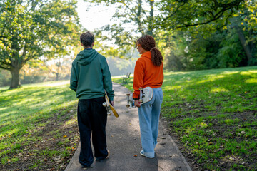 Friends walk in the park with skateboards in hand on a sunny day
