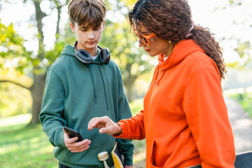 Teen and adult check phone outdoors during daytime in park with green trees