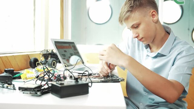 Caucasian boy fixing main board while study construction by using laptop analysis data. Young technician repairing and learning about using industrial structure at STEM technology class. Edification