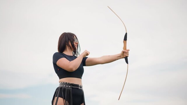 Focused woman with sharp aim, Determined female archer targeting skyward with precision, Fierce and confident female archer aligns her bow carefully aiming directly at her target amidst open sky