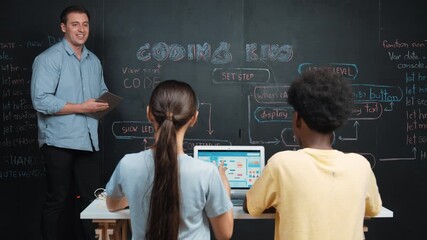 Professional teacher holding tablet while explain about programming system at blackboard while teenager with mixed raced working on laptop by coding program in back view at STEM class. Edification - Powered by Adobe