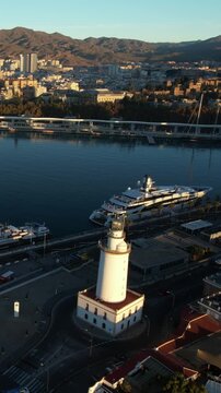 Malaga Spain aerial view featuring la farola lighthouse port yachts cityscape and mountains during early morning golden hour
