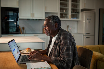 Senior man using laptop at home kitchen table