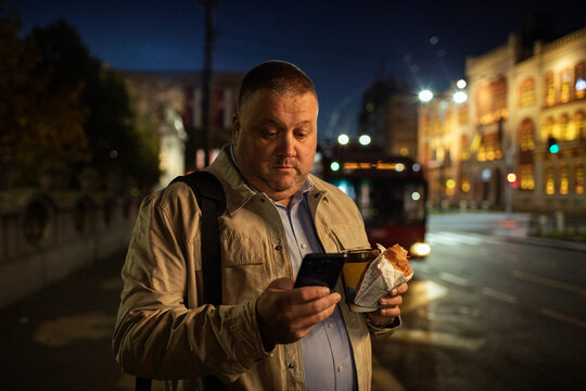 Middle-aged man using smartphone at city bus stop at night