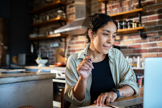 Young woman working on laptop in home kitchen