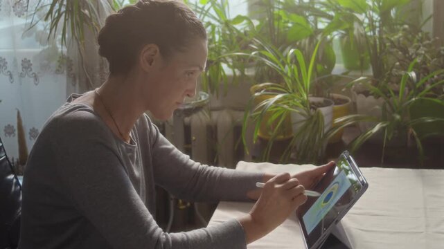Woman drawing a peacock feather on a tablet while sitting at a table in a room