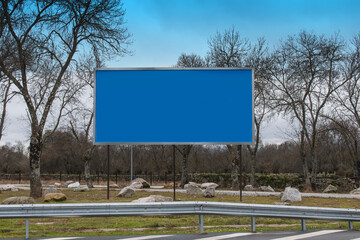Billboard with a blue background in a meadow with trees near a road