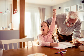 Grandfather helping granddaughter with homework at home