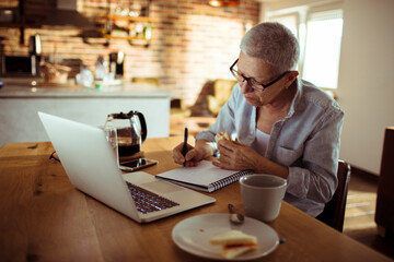 Senior woman writing notes while working in the home kitchen