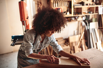 Female woodworker sanding plank in carpentry workshop