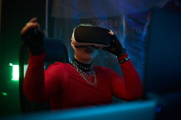 Young adult Caucasian woman wearing virtual reality headset sitting at desk interacting with digital interface in dark room suggesting hacker or cybersecurity activity