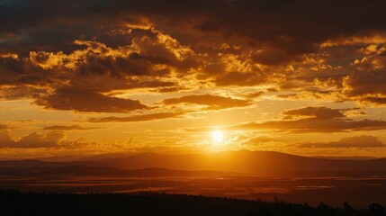 A vibrant sunset casts golden hues over distant mountains and fields, creating a serene and picturesque landscape.