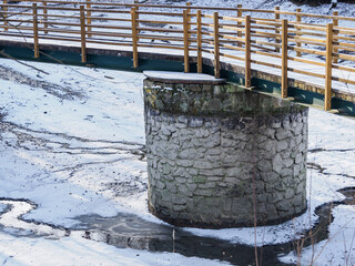 An exposed part of a concrete bridge pillar by a pond that has been drained.
