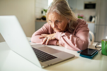 Senior woman struggling with laptop at home kitchen