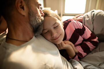 Father cuddling daughter in bed at home