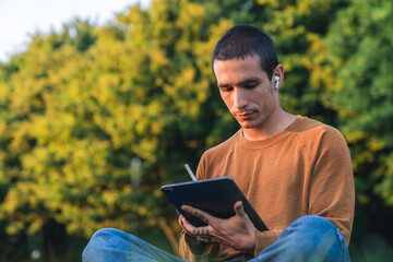 Fototapeta premium Young creative artist drawing on a digital tablet, enjoying the peace of nature in a park