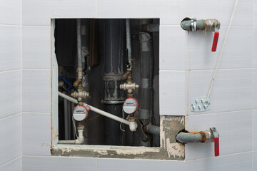 Open tiled wall access hatch reveals water meters, shutoff valves and corroded pipes after leak, urgent home plumbing repair.