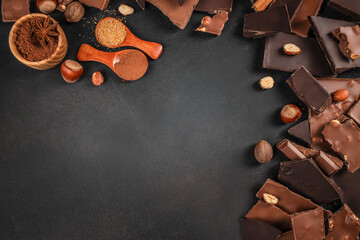 Chocolate pieces with cocoa powder and spices on dark background with copy space