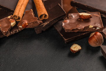 Chocolate pieces with hazelnuts and cinnamon sticks on dark background
