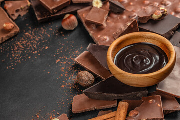 Chocolate sauce in wooden bowl with chocolate pieces on dark background with copy space