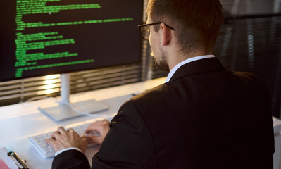 Programmer man coding at computer in office. A focused developer types at a keyboard as a bright screen shows software code in a clean workspace. Concept of modern professional software work.