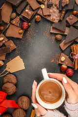 Hands holding cup of hot chocolate with chocolate pieces on dark background with copy space