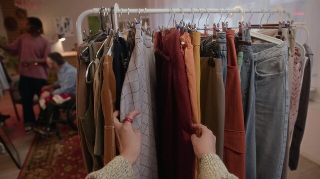 POV of unrecognizable customer hands browsing and choosing vintage clothing items from rack in inclusive second hand store, exploring fashion in inclusive thrift store