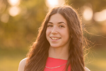 beautiful teenage brunette girl with long hair, smiling, looking at the camera during a summer walk
