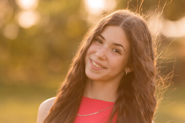 beautiful teenage brunette girl with long hair, smiling, looking at the camera during a summer walk