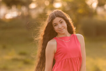 beautiful teenage brunette girl with long hair, smiling, looking at the camera during a summer walk
