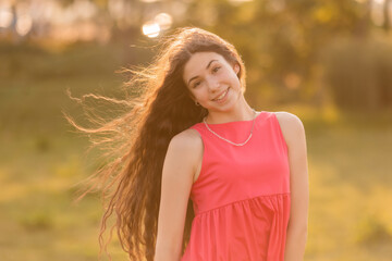 beautiful teenage brunette girl with long hair, smiling, looking at the camera during a summer walk