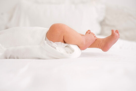 A newborn in a diaper is lying on white bedding on the bed. Close-up of a baby's legs with peeling skin. Caring for the delicate skin of Infants