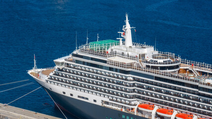 High-angle closeup of a luxury cruise ship docked in port. Aerial view of a cruise boat with many deck levels, balconies, and the sleek white bridge against the deep blue sea. Ship docked at the port