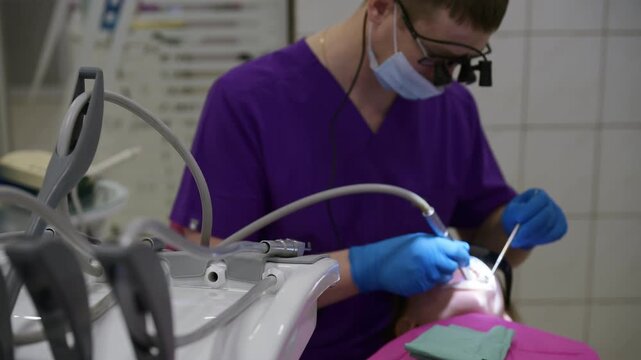 A dental professional in purple scrubs carefully treats a patient, using precise tools and ensuring a calming, safe environment with protective gear.