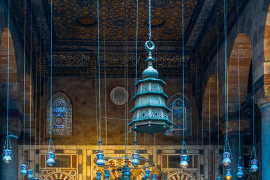 Intricate ceiling design of Madrasa Al-Kamil Ayyub in Cairo, featuring ornate patterns and hanging lamps. The vibrant colors and details reflect Islamic architecture.