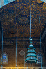 Intricate ceiling design of Madrasa Al-Kamil Ayyub in Cairo, featuring ornate patterns and hanging lamps. The vibrant colors and details reflect Islamic architecture.