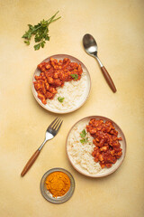 Indian chicken curry served with white rice and turmeric on yellow background top view