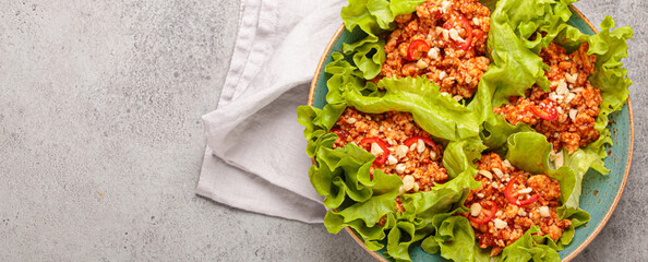 Lettuce wraps filled with minced meat and topped with peanuts and chili pepper flakes on a plate